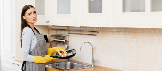 Exhaused Housewife Concept. Unhappy girl doing the dishes in protective gloves and apron, tired of...