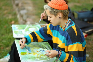 two young and innovative female artists conducting an outdoor painting lesson. Surrounded by...