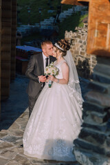 A bride and groom are kissing in front of a stone wall. The bride is wearing a white dress and the groom is wearing a suit