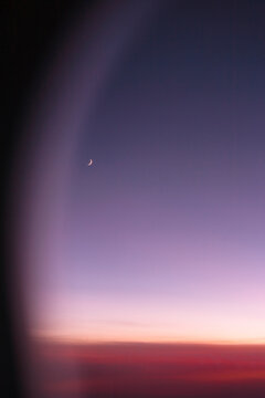 View of a thin sliver of moon in the sky from plane window.