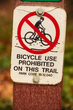 Close up of a bicycle use prohibited sign by a trail, note of a park code. 