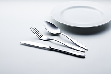 Silver colored cutlery such as spoons, forks, knives, cups and plates photographed against a white background