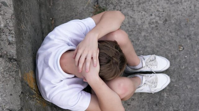 Sad boy sitting outside in a bad mood after school. Childhood depression, headache and migraine, bullying.