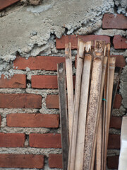 A pile of old, split bamboo in the background of a brick wall that will be used to make a fence.
