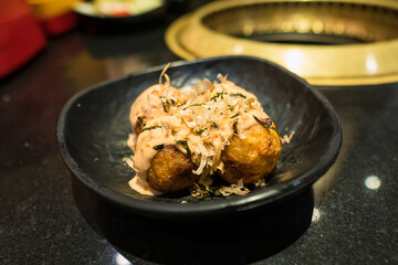 Delicious Japanese Takoyaki Balls with Toppings in a Black Bowl on a Restaurant Table
