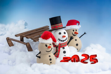 A joyful snowman and two sandy snowmen pose together for a Christmas and New Year celebration.  Lot of snow, blue sky, this mix of winter and beach vibes brings a fresh holiday twist with a sled.
