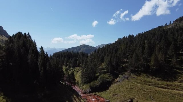 R&iacute;o Arriu Unh&ograve;la de color rojizo en Vielha, Lleida, rodeado de bosques y pastos verdes, visto desde un dron