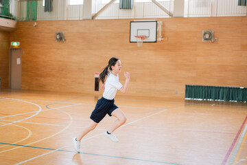 学校の体育館の中で走る体操着姿の女子生徒
