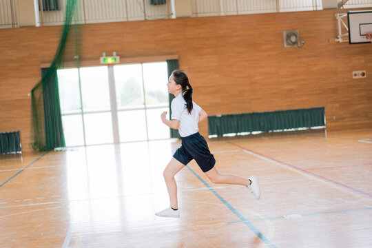 学校の体育館の中で走る体操着姿の女子生徒
