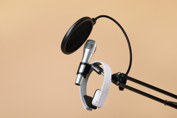 Stand with microphone, headphones and pop filter on beige background, space for text. Sound recording and reinforcement