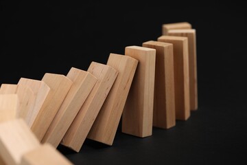 Domino effect. Wooden blocks falling on black background, closeup