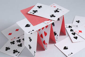 Collapsed house of playing cards on light grey background, closeup