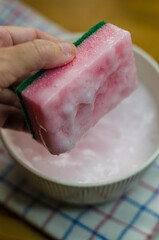  hand holding dishwashing sponge soaked in a solution of soda, vinegar and soap. High quality photo