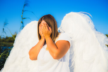 Young woman with angel wings and white t-shirt covering her face with hands expressing sadness or...