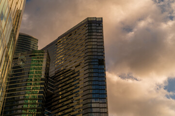 Fototapeta premium Skyscrapers in business district against blue sky. Looking Up high-rise office buildings. Evening time, sunset. Orange, yellow and gold shades of color. Angled view.