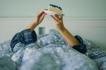 woman eating a Cheesecake in Pajamas for a Cozy Dessert Moment in bedroom . High quality photo