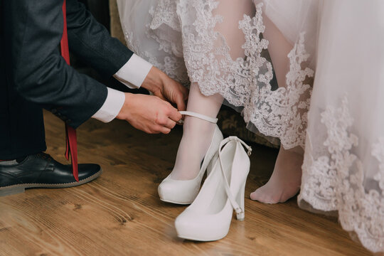 A man is helping a woman put on her wedding shoes. The man is wearing a suit and tie. The woman is wearing a white dress