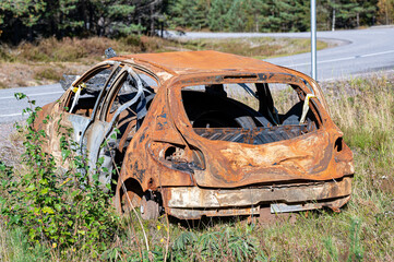 Burned out car starting to rust near road