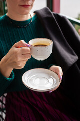 Female hands holding a white cup. The woman is drinking coffee.