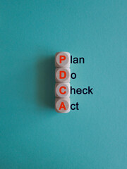 Wooden cubes with the orange words PDCA. It is an abbreviation for Plan, Do, Check, Act as eye-catching image. Beautiful blue background. Business concept.