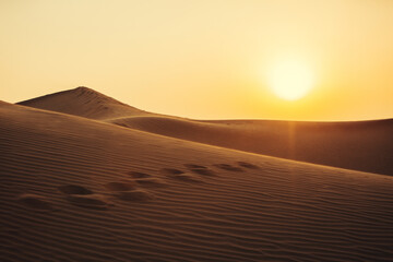 Views of the Dubai desert at sunset, footprints in the sand, with wind sweeping grains off the dunes.