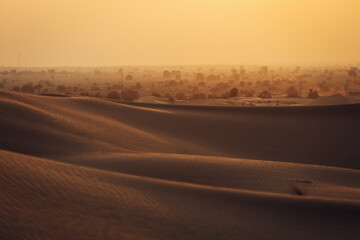 Views of the Dubai desert at sunset, footprints in the sand, with wind sweeping grains off the dunes.