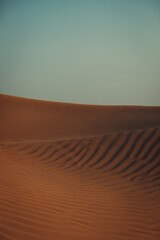 Views of the Dubai desert at sunset, footprints in the sand, with wind sweeping grains off the dunes.