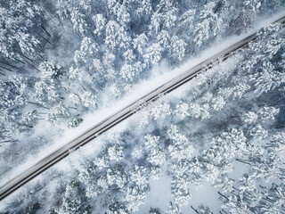 Aerial view of a snow-covered road meandering through a dense forest during winter, showcasing the...