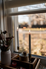 window with burning burning candle and autumn leaves in the background