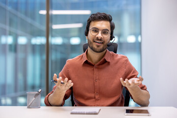 Hispanic businessman with headset in office setting, confidently engaging in conversation. Glasses...