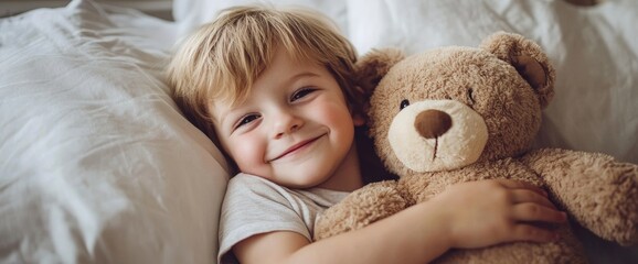A young child with a bright smile holds a soft teddy bear tightly in a comfortable bed surrounded by fluffy pillows on a sunny morning