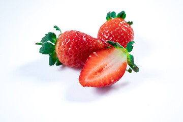 Two whole strawberries and one half-sliced strawberry placed on a white background, showing vibrant red color and juicy texture. Perfect for healthy eating, fresh produce, and food-related visuals