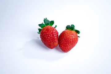 Two whole strawberries and one half-sliced strawberry placed on a white background, showing vibrant red color and juicy texture. Perfect for healthy eating, fresh produce, and food-related visuals