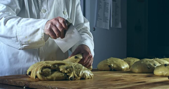 Super slow motion close up of artisan baker dividing raw dough with chocolate pieces while kneading for homemade Italian panettone on rustic wooden table in bakery kitchen at 1000 fps.
