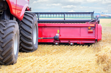 Massive combine harvester in golden wheat field, cutting crops, close up of machinery and tires,...