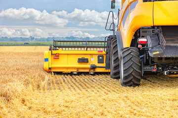 Harvesting machinery in golden wheat field under clear sky, agricultural equipment at work, rural landscape, farming concept