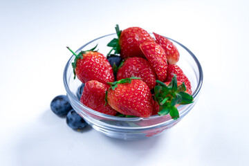 A bowl of fresh strawberries and blueberries on a white background, highlighting the vibrant red and deep blue colors of the berries. Perfect for promoting healthy eating and antioxidant-rich foods