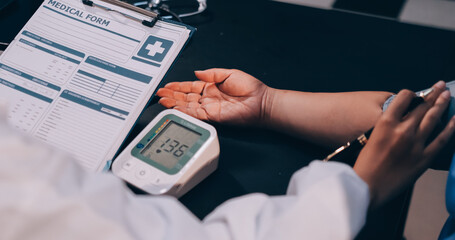 A doctor taking a patient's blood pressure. The patient's arm is equipped with a blood pressure...