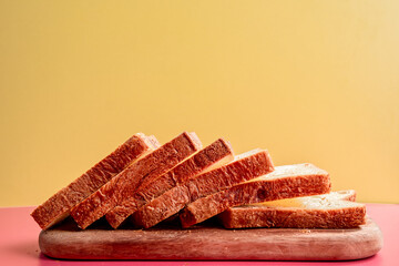 A stack of fresh, thick-cut bread slices neatly arranged on a wooden board against a vibrant yellow...