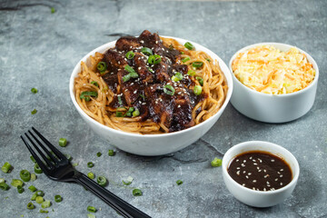 Teriyaki Grilled Chicken Noodles with green onion, spicy sauce, cabbage salad and fork served in bowl isolated on grey background side view of japanese food