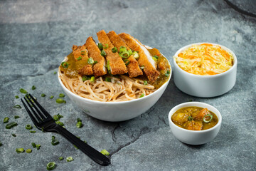 Katsu Chicken Noodles with potato curry, cabbage salad, green onion and fork served in bowl isolated on grey background side view of asian food