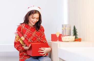 Happy Asian beautiful woman. Pretty girl sitting on chair wearing santa hat red long sleeve knitted sweater smiling with gift box present enjoy party Christmas eve Happy New Year celebration holiday.