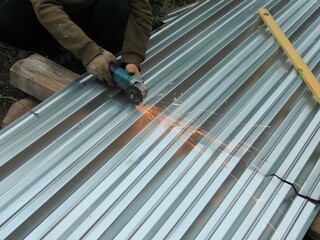 hands of a builder holding a grinder and cutting a sheet of metal on the ground with sparks, use of hand tools in processing iron material, iron cutter in the process of work