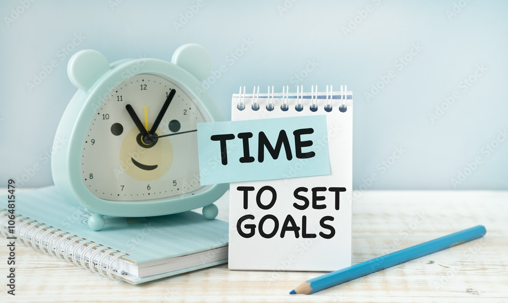Poster paper with text time to set goals and pen, notebook, alarm clock.