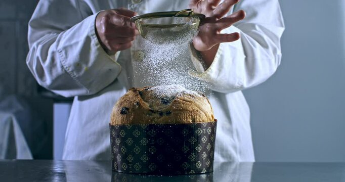 Super slow motion close up of dusting powdered sugar over freshly baked Italian panettone on rustic wooden table in bakery kitchen at 1000 fps.