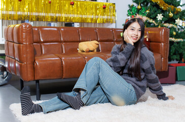 Cheerful young beautiful asian women. Cute female  wearing deer horns and long sleeve knitted sweater sitting on carpet smile posing enjoy a party, Happy New Year celebration Christmas holiday concept