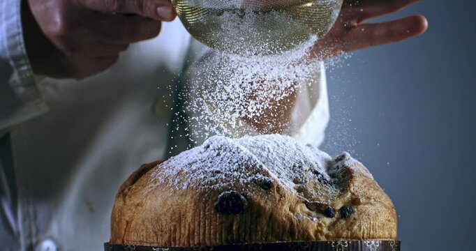 Super slow motion macro of dusting powdered sugar over freshly baked Italian panettone on rustic wooden table in bakery kitchen at 1000 fps.