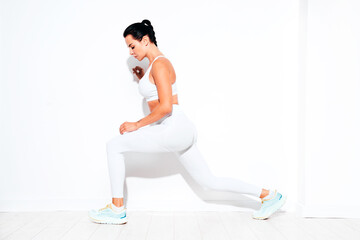 Fototapeta premium Fitness confident woman in white sports clothing. Sexy young beautiful model with perfect body. Female isolated on white wall in studio. Stretching out before training, makes lunges