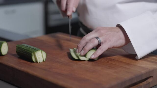 A static shot of a chef expertly slicing multiple cucumbers lengthwise on a cutting board. Perfect for culinary content, highlighting knife skills and food preparation techniques in a pro kitchen