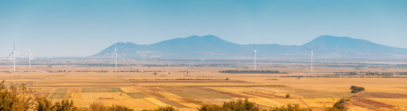 Scenic landscape of Vrsac, Serbia, featuring majestic mountains and a picturesque farm with wind turbines harnessing renewable energy
